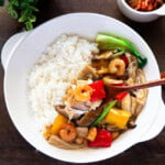 Holding a bite-sized portion of shrimp, red bell pepper, mushrooms, and rice on a wooden spoon.