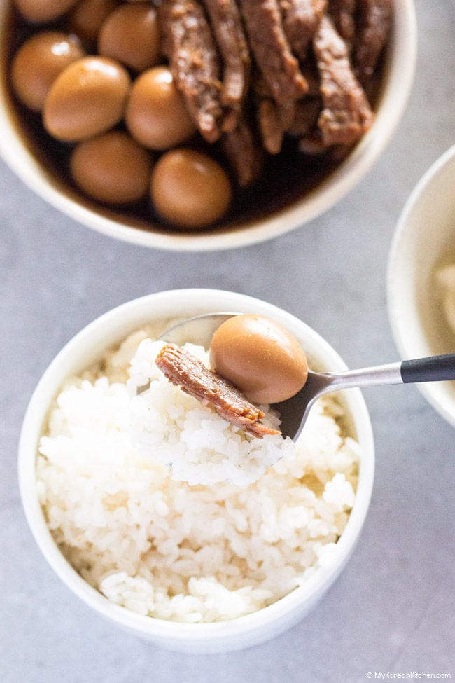 Soy braised beef and quail egg scooped with a spoon over a bowl of white rice.