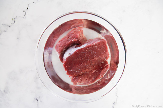 Soaking beef in a clear bowl of water.