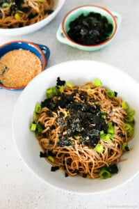 Soba noodles served in a bowl, garnished with seasoned seaweed and green onions.