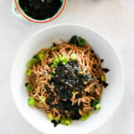 Top down image of soba noodles served in a bowl, garnished with seasoned seaweed and green onions.