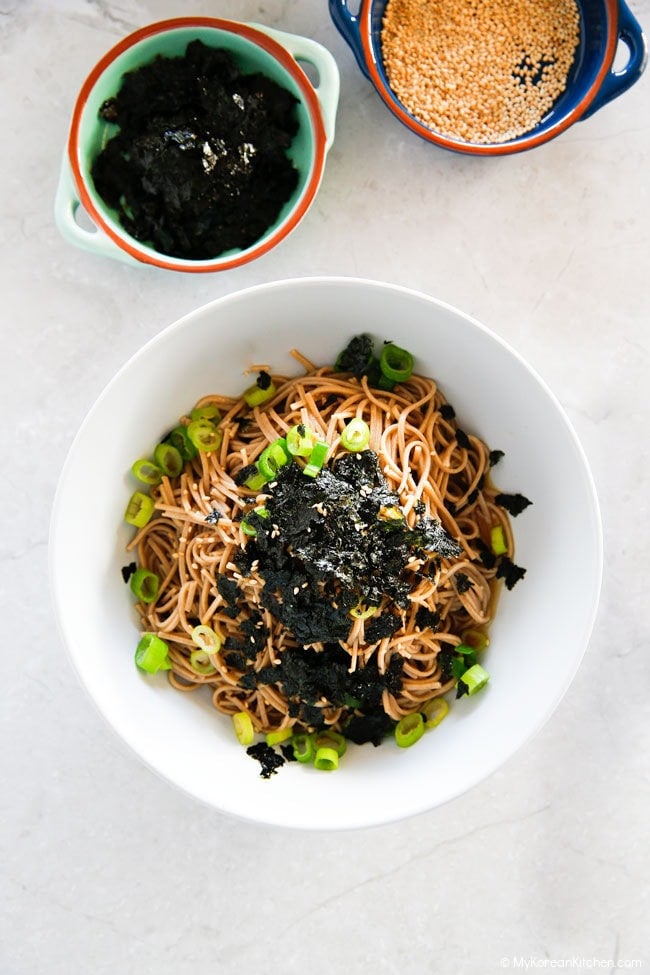 Top down image of soba noodles served in a bowl, garnished with seasoned seaweed and green onions.