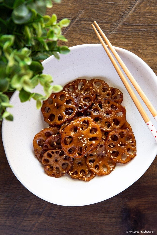braised lotus root in an oval-shaped bowl with chopsticks resting on top