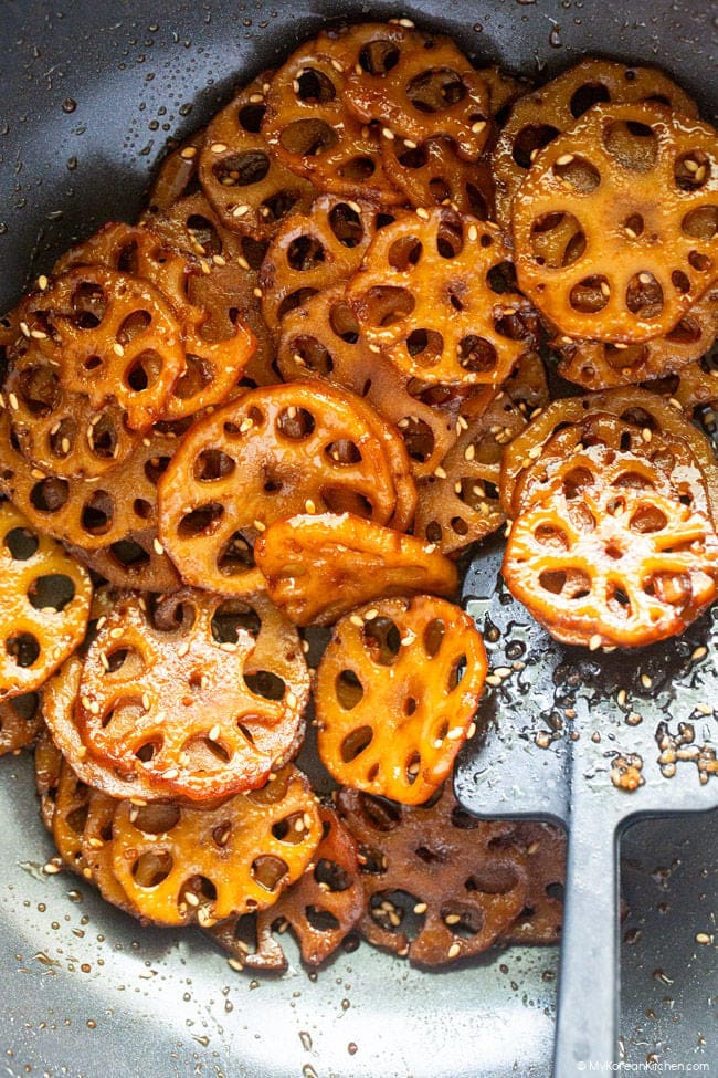 soy-glazed lotus root in a nonstick wok with a black spatula resting inside