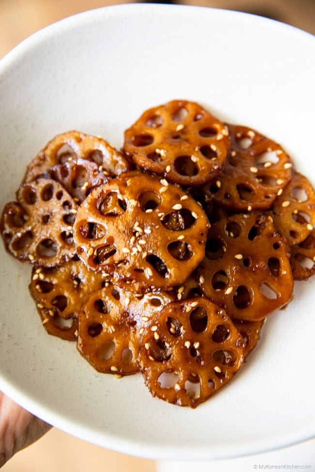 a hand holding an oval-shaped bowl containing braised lotus root