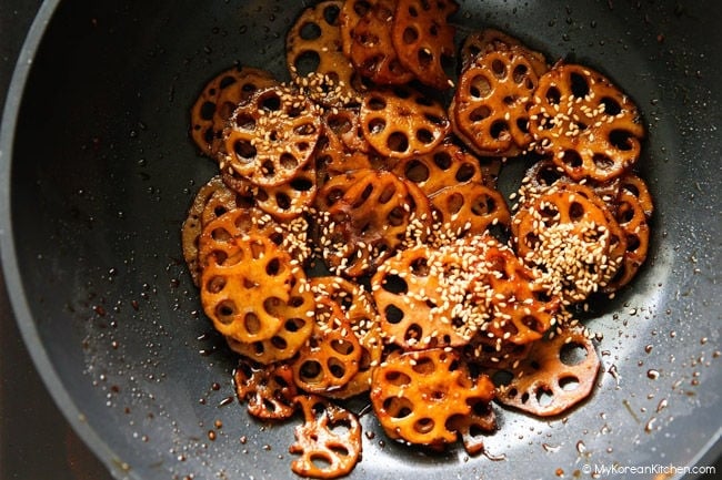 braised lotus root resting in the wok, scattered with sesame seeds