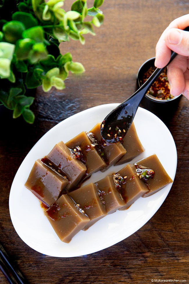 Drizzling acorn jelly salad sauce with a black spoon over sliced acorn jelly.