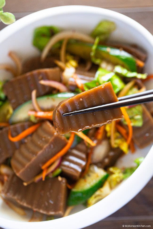 Holding a piece of seasoned acorn jelly with wooden chopsticks.