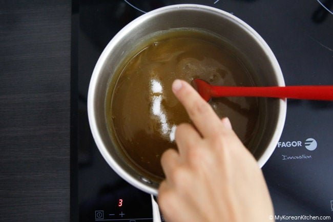 Stirring Korean acorn jelly in a saucepan with salt sprinkled on top.