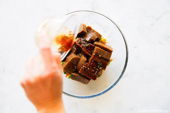 Adding the remaining salad sauce over sliced acorn jelly in a mixing bowl.