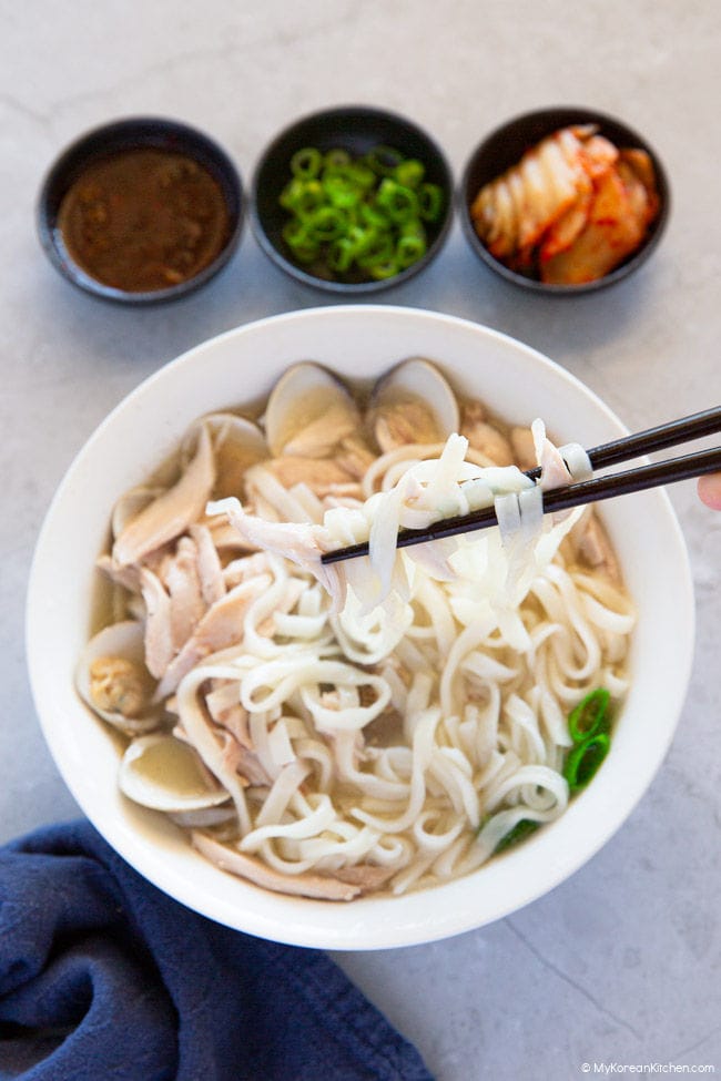 Holding kalguksu noodles with chopsticks over a white bowl of soup.
