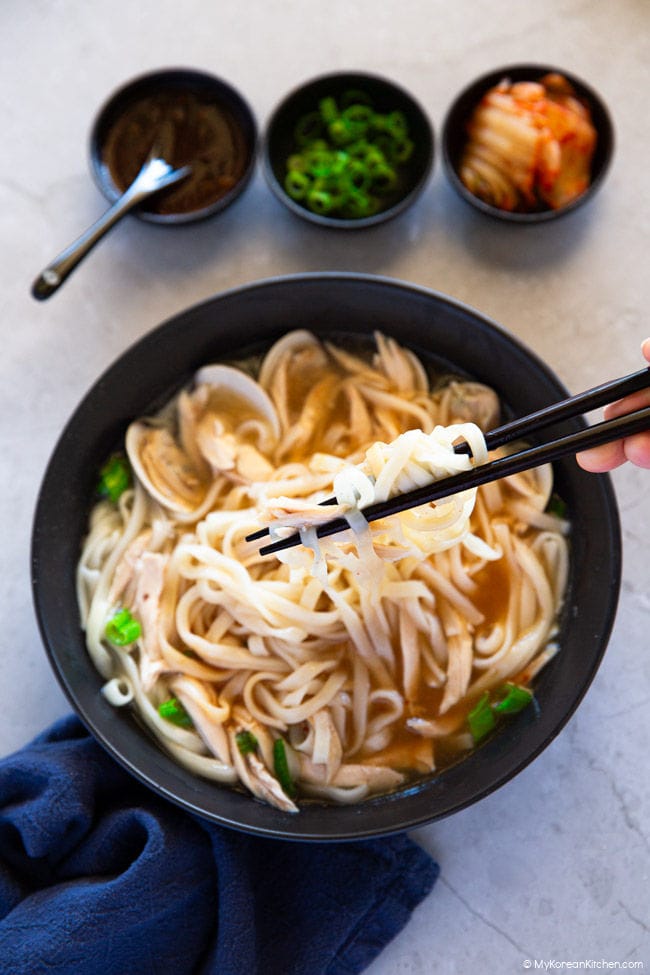 Holding kalguksu noodles with chopsticks over a black bowl of soup.