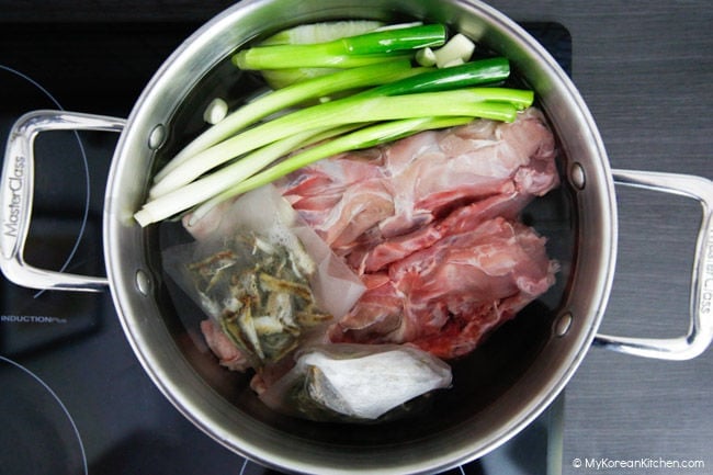 Chicken stock ingredients, including a chicken frame and green onions, are in a large stock pot, ready to boil.
