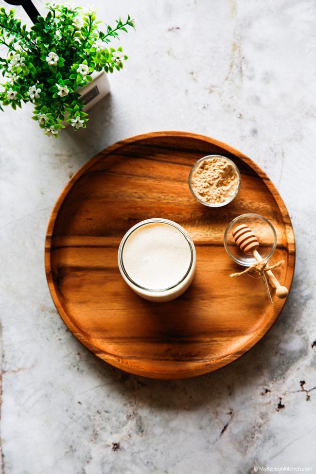 Gambar misugaru latte dari atas ke bawah di atas nampan kayu, dengan semangkuk kecil bubuk misugaru dan sendok madu dekoratif di sampingnya.