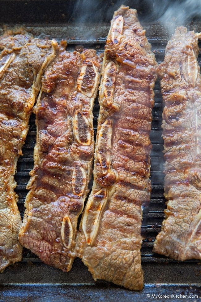 LA galbi grilling over a wavy cast iron plate, sizzling and caramelizing on the surface