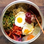 bibimbap ingredients in a large stainless steel bowl, including a sunny side egg, zucchini, spicy radish salad, bean sprout salad, and gochujang.