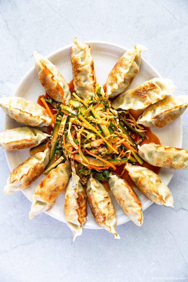 Pan-fried dumplings arranged around a seasoned salad on a large plate.