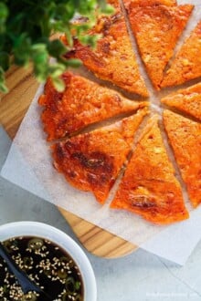 Sliced kimchi pancake into bite-sized pieces, served on a wooden board with dipping sauce.