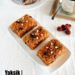 Yaksik dessert elegantly served on a rectangular white plate, with an additional three individually wrapped pieces arranged in the background on a matching round plate.