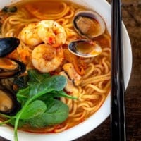 A bowl of jjampong topped with prawns, mussels and littleneck clams.