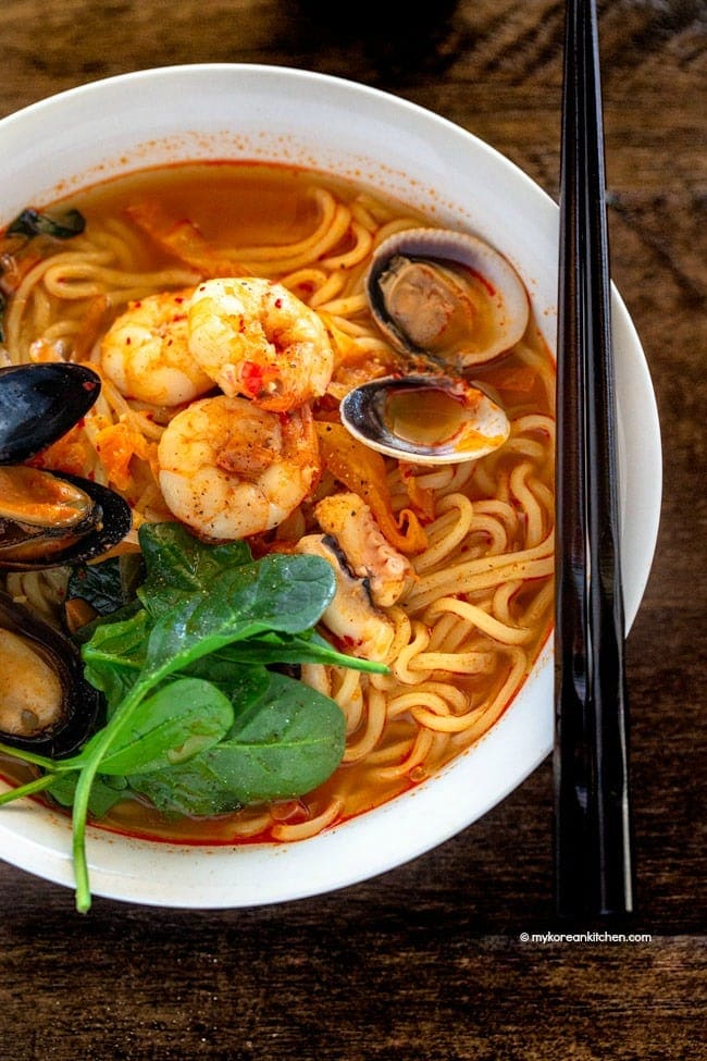 A bowl of jjampong topped with prawns, mussels and littleneck clams.