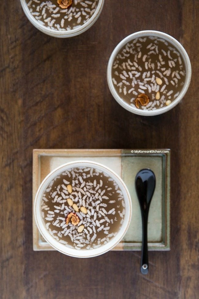 An overhead shot of bowls of sikhye. The drink is topped with pine nuts and rice.