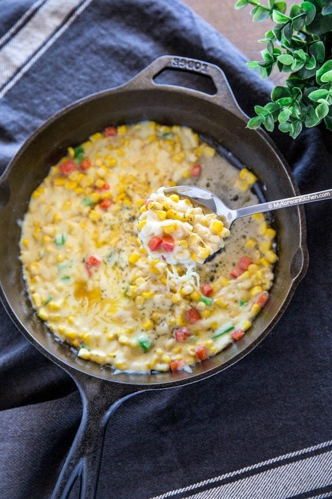 Korean corn cheese is served in a skillet and is scooped with a spoon.