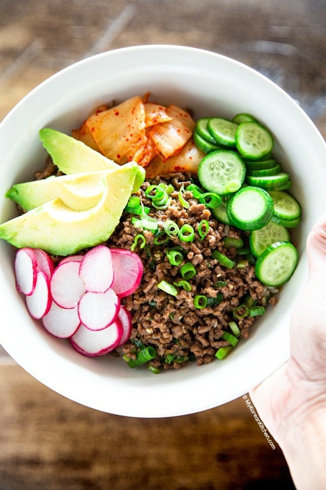 Korean beef bowl served with sliced pink radishes, avocados, cucumbers, and kimchi