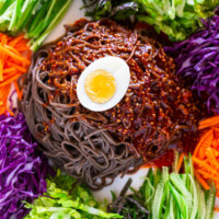 close up photo of spicy noodle salad featuring halved boiled egg on top of noodles