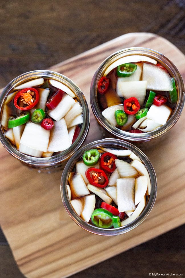 Top-down shot of three open jars filled with chopped onions, sliced chili peppers, and brine.