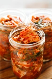Holding kimchi with wooden chopsticks over a glass kimchi jar