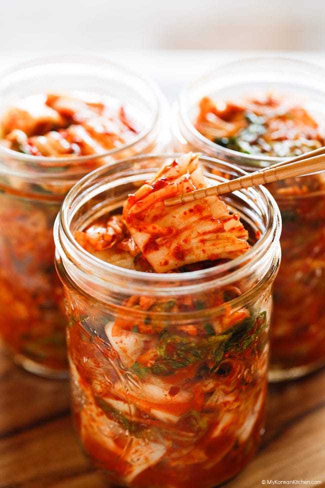 Holding kimchi with wooden chopsticks over a glass kimchi jar