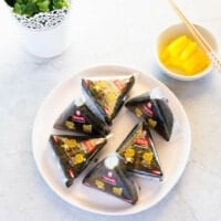 Six triangle kimbap served on a plate, yellow pickled radish in the background