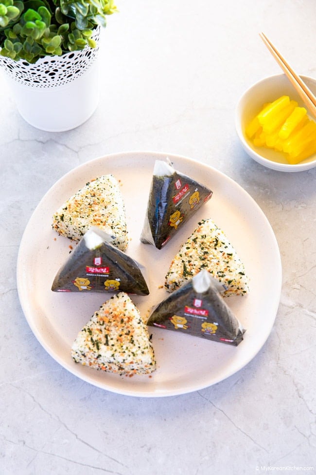 Three triangle kimbap, covered with plastic film and the other three with rice seasoning (furikake).