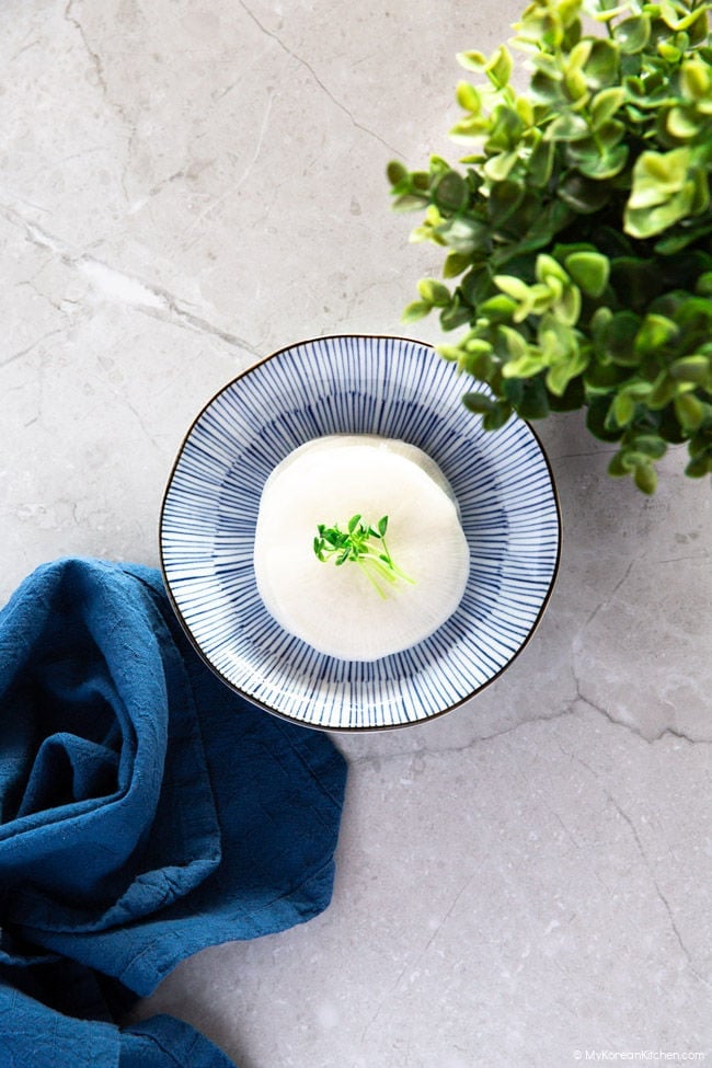 Pickled white radish served on a blue plate. Decorated with green sprouts.