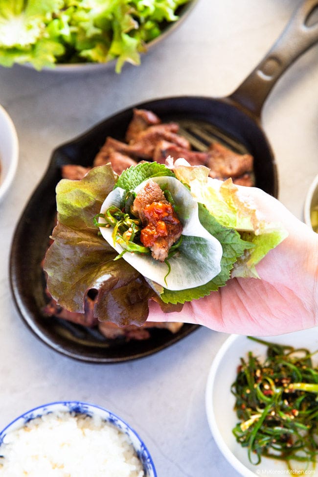 Holding a lettuce wrap - lettuce, pickled radish, BBQ pork, and dipping sauce on the palm.