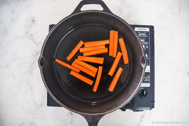 Cooking the carrot sticks in a frying pan.