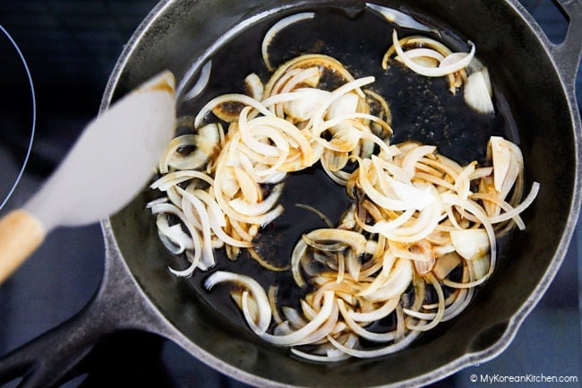Stir-frying onions with sauce in a skillet.