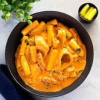 Rose tteokbokki is served in a black pasta bowl, accompanied by slices of yellow pickled radish.