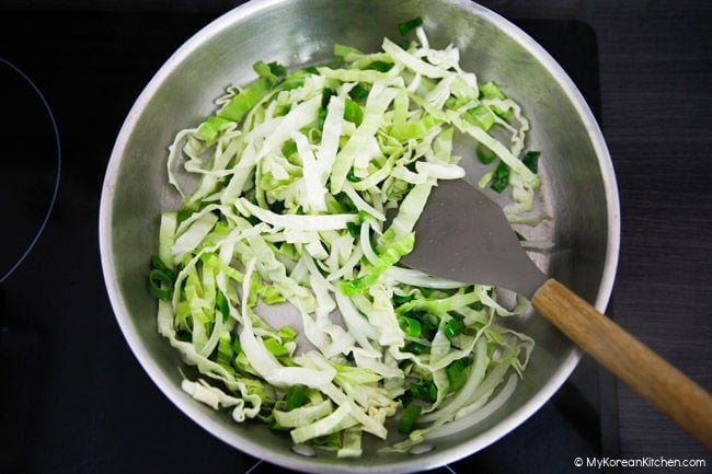 Stir-frying onion, green onion and cabbage in a stainless-steel pan.