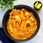 Rose tteokbokki is served in a black pasta bowl, accompanied by slices of yellow pickled radish.