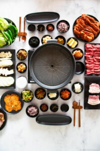 A vertical photo of a Korean BBQ table set up with various side dishes and meat.
