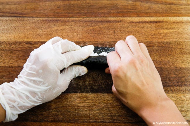 Rolling the kimbap ingredients tightly on the wooden board.