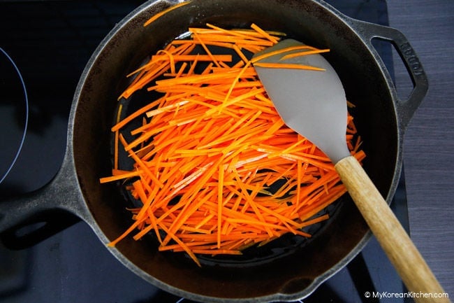 Stir frying fresh julienned carrots in a skillet with a pinch of salt.