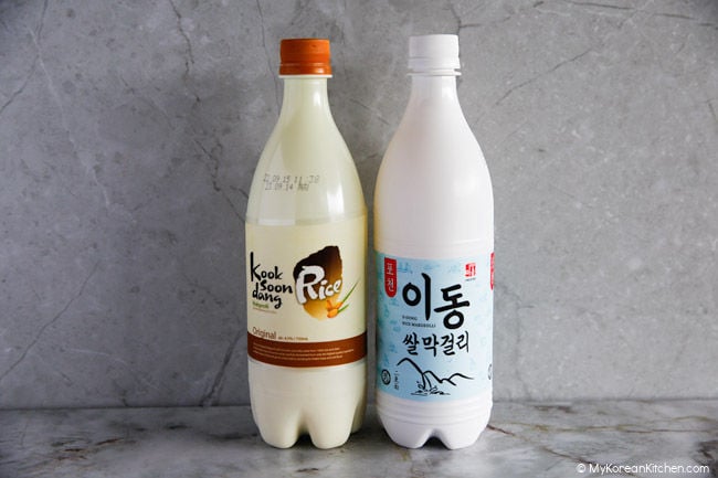 Two bottles of makgeolli positioned against a wall.