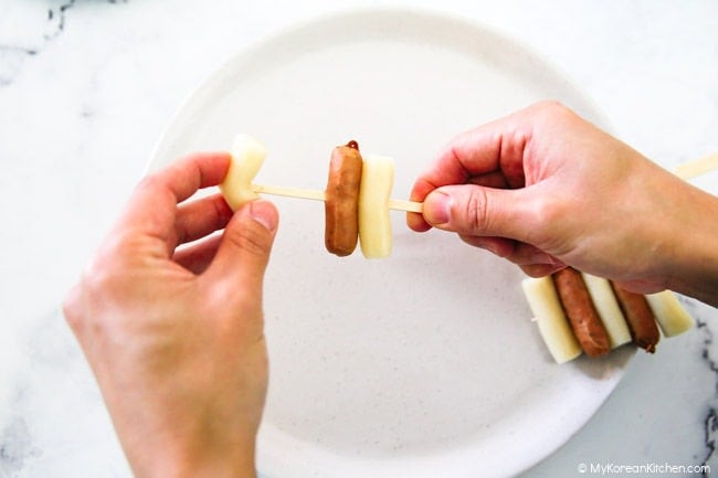 Threading the rice cake and the mini sausages onto wooden skewers.