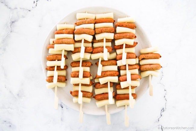 A large plate piled with sausage and rice cake skewers