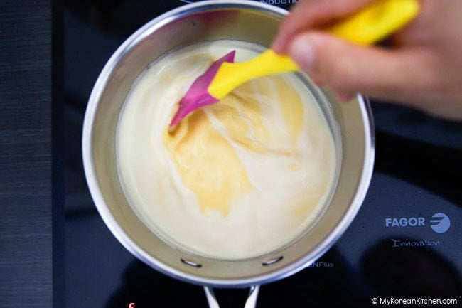 Stirring the custard mixture in a pot on the stove to thicken it.