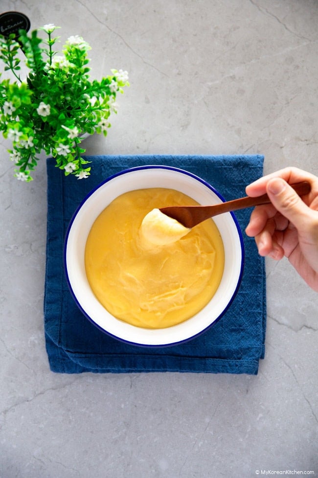 A hand holding a wooden spoon, scooping vanilla custard from a serving bowl.
