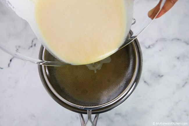 Straining the custard mixture into a stainless steel bowl.